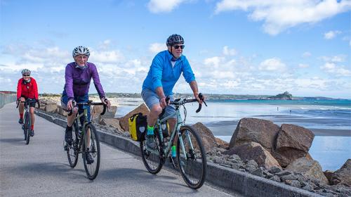 Cyclists riding along a path with the sea in the background